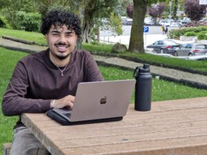 Ismail Karim, a SiPN Spring 2025 student, sitting at an outdoor table with his laptop and water bottle on the campus of Universidade Católica Portuguesa.
